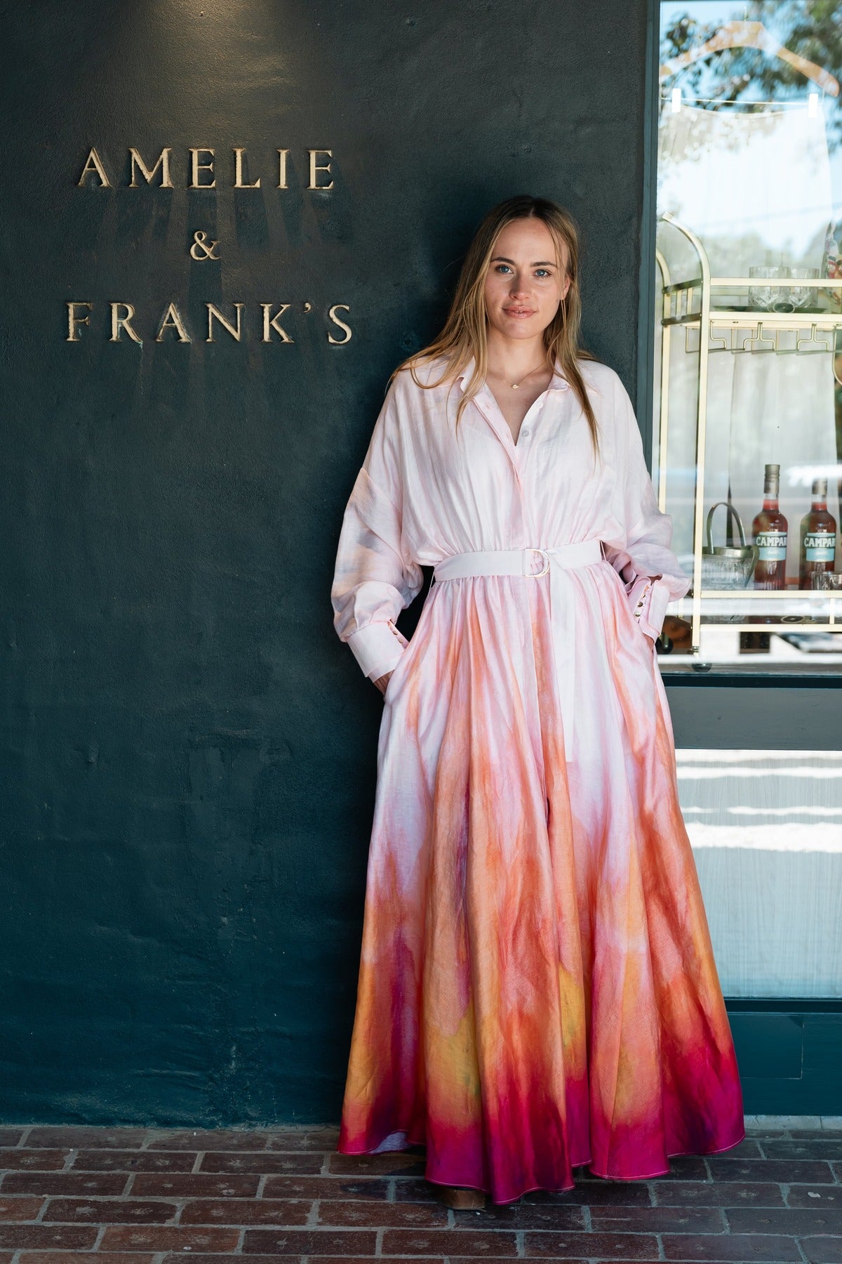 The Acler Driften maxi dress worn against the Amelie & Frank's signage wall at Red Hill, the ombre running from blush to flame at the hem