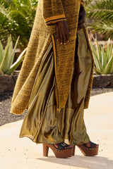 Leone trousers worn under a long olive knit cardigan, walking on a garden path