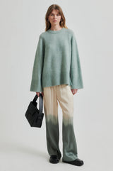 Second Female Avora Dip Dye Pants in agave green, worn by model with a green knit, front view