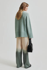 Second Female Avora Dip Dye Pants in agave green, worn by model with a green knit, back view