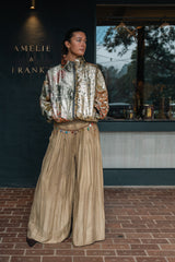 Model outside the Amelie & Frank's door in the wide beige trousers, worn with a metallic floral bomber