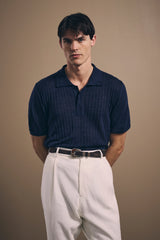 Navy Christian Kimber basketweave linen knit polo worn with ivory pleated trousers and a leather belt