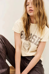 Model in the ecru tee with taupe BA&SH varsity print and brown leather trousers