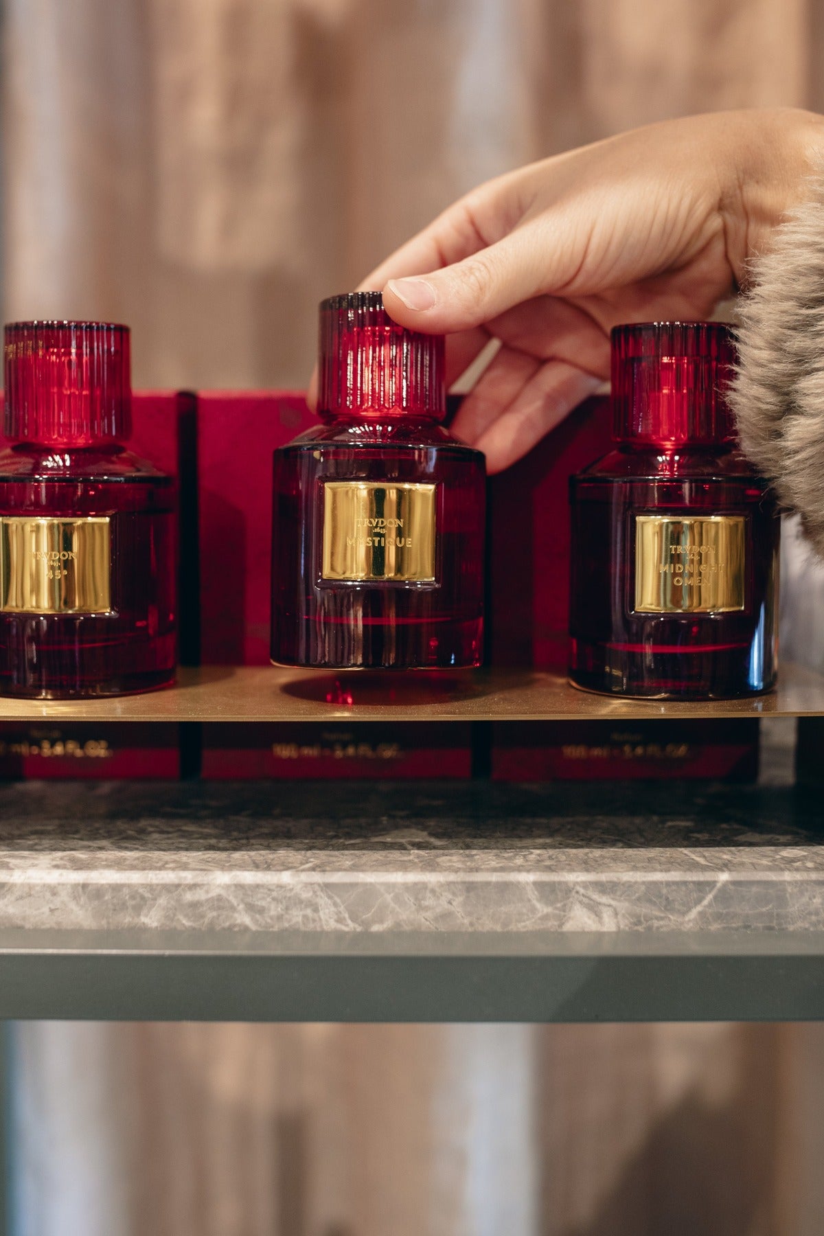 A hand reaching for a bottle on the fragrance shelf at Amelie & Frank's in Red Hill