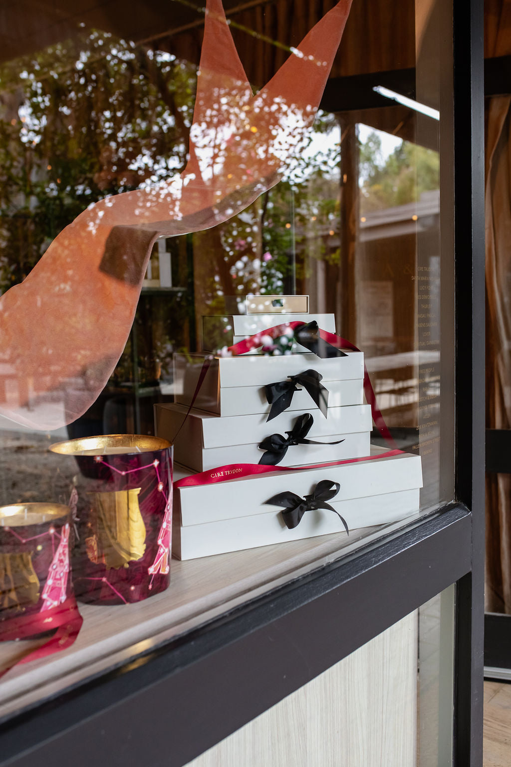 The Amelie & Frank's shop window at Christmas, white gift boxes tied with black ribbon stacked as a tree, Trudon constellation candles beside them