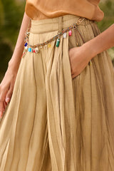 Close view of the charm and tassel chain, the front pleats and a hand in the pocket