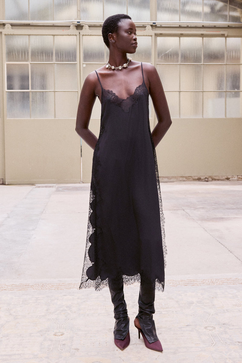 Black Balma slip worn over boots in a bright warehouse, front view