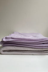 Amelie & Frank's Cashmere Throw in oatmeal, folded in a stack with a lavender throw
