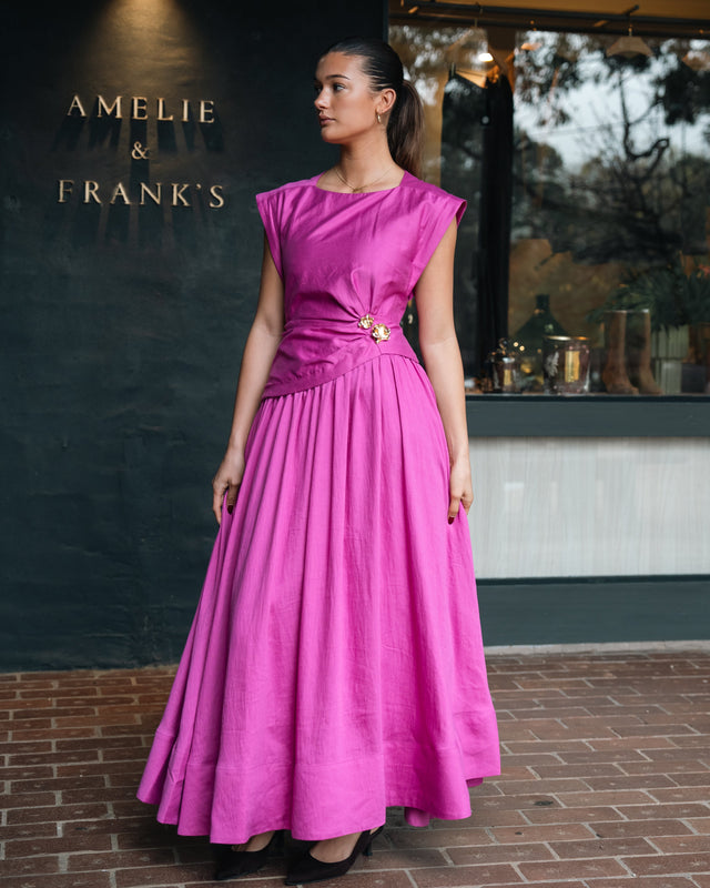 A model in a magenta dress in front of the Amelie & Frank's signage, gold lettering on the dark rendered wall