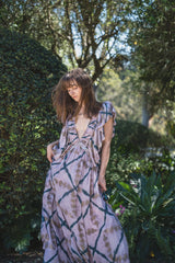 The Orma dress in lavender tie-dye, wind in the hair against a clipped hedge