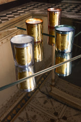 Trudon La Nuit des Glaces candles in silver, copper, gold and celadon mirrored glass, lit on a glass table and reflected below