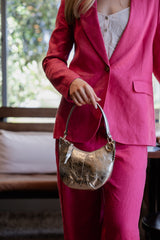 Close view of the single-button Crest jacket in rhubarb pink, a gold crescent bag held at the hip