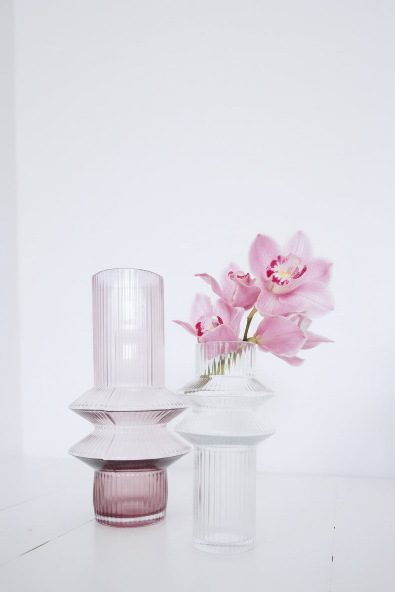 Marmoset Found Aswan Vase Small in clear glass, holding pink orchids beside a pink Aswan vase